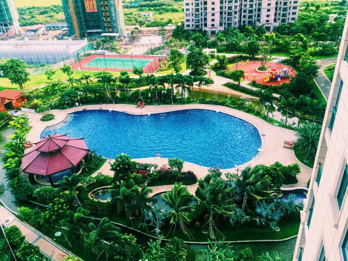 Vista aérea de piscina, quadra de tênis e área verde de um condomínio