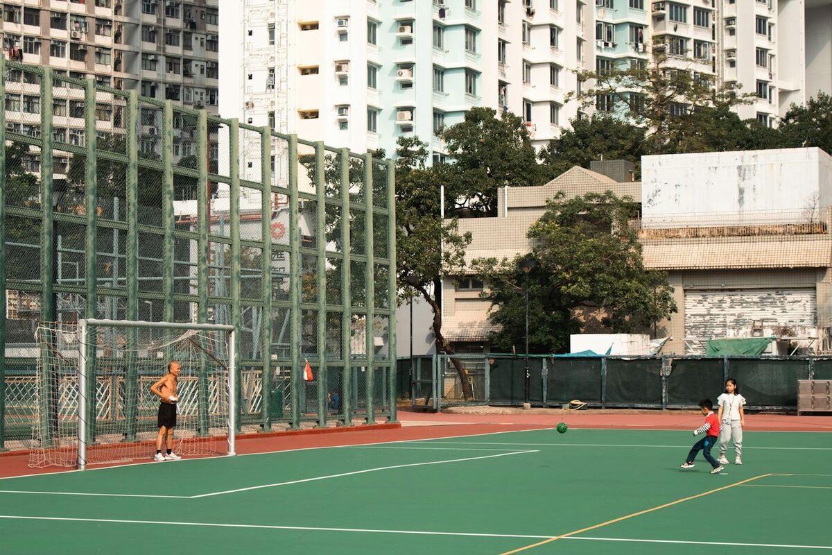 Pessoas jogando futebol em uma quadra com prédios ao fundo